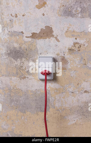 Corda di colore rosso e tappo in un bianco presa elettrica su una piscina intonacata parete di mattoni Foto Stock