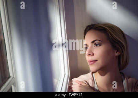 Donna seduta sul davanzale, guardando fuori della finestra Foto Stock