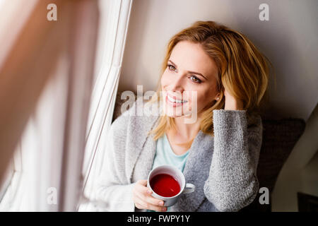 Donna sul davanzale tenendo una tazza di tè Foto Stock