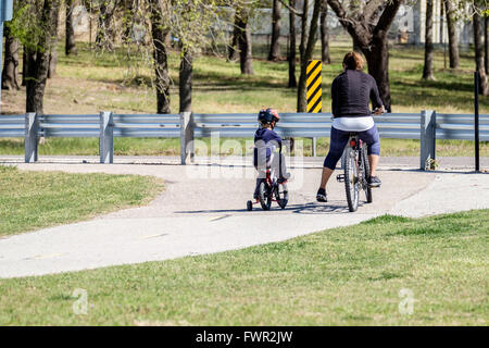 Una madre caucasica e piccolo figlio correre in bici insieme sui sentieri del lago Overholser, Oklahoma City, Oklahoma, Stati Uniti d'America. Foto Stock