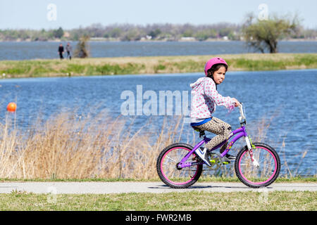 Una piccola ragazza ispanica cavalca la sua bicicletta per esercitare sul lago Overholser sentieri nella città di Oklahoma, Oklahoma, Stati Uniti d'America. Foto Stock