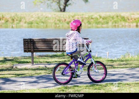 Una piccola ragazza ispanica cavalca la sua bicicletta per esercitare sul lago Overholser sentieri nella città di Oklahoma, Oklahoma, Stati Uniti d'America. Foto Stock