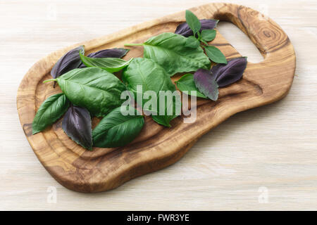 Cimelio di basilico sul legno d'ulivo cutboard. La cultivar compresi Genovese, basilico santo, spice globo. Foto Stock