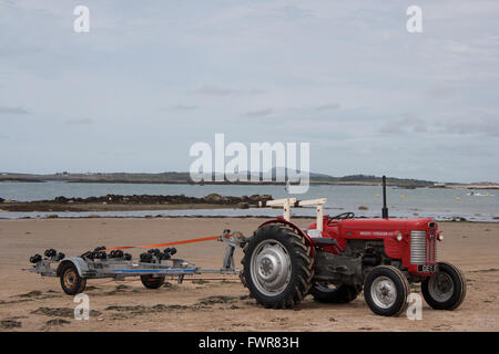 Un rosso trattore Massey Ferguson con vuoto rimorchio barca sulla spiaggia di Rhosneigr, Anglesey, Galles, UK. Foto Stock