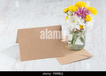 La molla bouquet di fiori in un vaso vaso con carta kraft nota e la busta su un legno bianco sfondo rustico Foto Stock