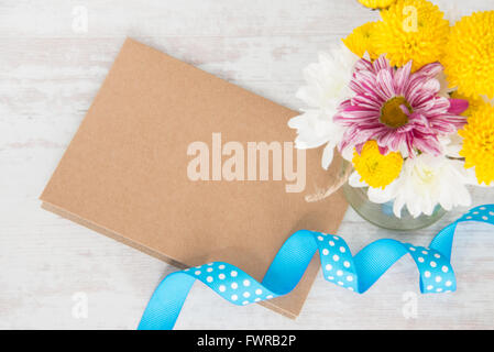 La molla bouquet di fiori in un vaso vaso con carta kraft nota, Busta e puntini blu nastro su un legno bianco sfondo rustico Foto Stock