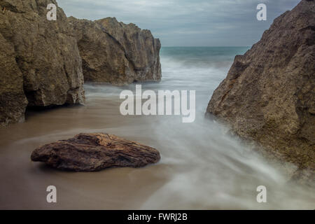 Una lunga esposizione di driftwood tra le rocce su una spiaggia in Narbonne, Francia. Foto Stock