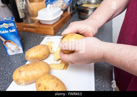 Un close-up di mani femminili sbucciare le patate in una cucina Foto Stock