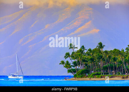 Barca a vela di fronte spiaggia di sabbia dorata con palme sulla costa di Maui con vista di Molokai in background Foto Stock