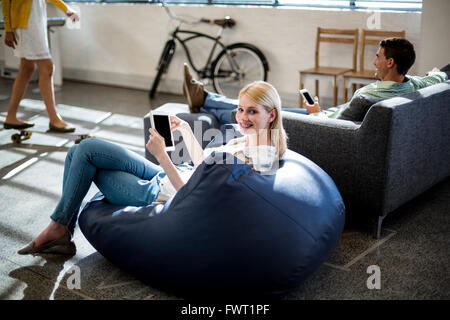 Giovane donna seduta su un bean bag holding tavoletta digitale Foto Stock