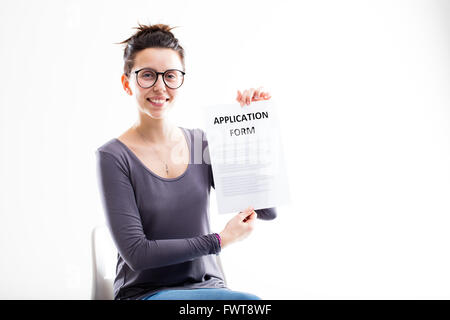 Donna con gli occhiali che mostra un modulo di domanda e sorridente seduto su un bianco sedia ufficio Foto Stock