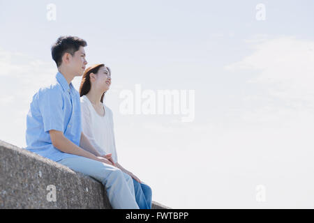 Un giovane giapponese giovane seduto sul muro di cemento in riva al mare Foto Stock