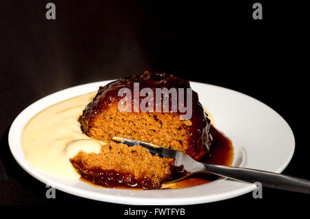 Sticky toffee pudding e crema pasticcera- Studio shot con uno sfondo nero Foto Stock