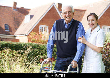 Accompagnatore Senior aiuta l uomo a camminare nel giardino con telaio a piedi Foto Stock