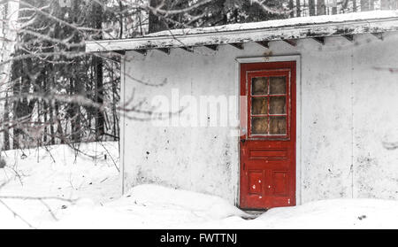 Semplice, vecchio capannone bianco, senza finestre tranne coperto in vetro rosso pallido porta, paese vecchio utility storage casolare immerso nella neve. Foto Stock
