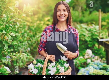 Felice giovane fioraio lavorando in una serra a un vivaio fresca raccolta fiori bianchi in un cesto di vimini in vendita nel suo negozio Foto Stock