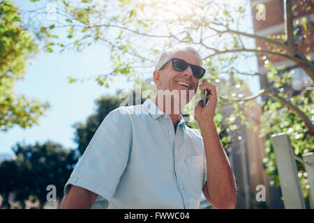 Ritratto di felice uomo maturo parlando al telefono cellulare all'aperto nella città in una giornata di sole. Senior uomo caucasico rendendo chiamata telefonica Foto Stock