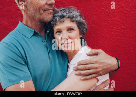 Ritratto di felice donna matura abbracciando il marito contro lo sfondo di colore rosso. Affettuosa giovane insieme contro lo sfondo rosso Foto Stock