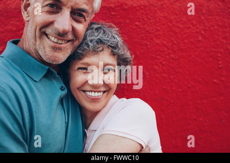 Ritratto di Allegro Coppia di mezza età che abbraccia ogni altra contro lo sfondo di colore rosso. Uomo maturo e la donna insieme contro w rossa Foto Stock