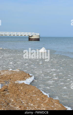 Una vista del molo sul Lago Huron in Oscoda contro un cielo azzurro e la fusione della neve e del ghiaccio di inverno Foto Stock