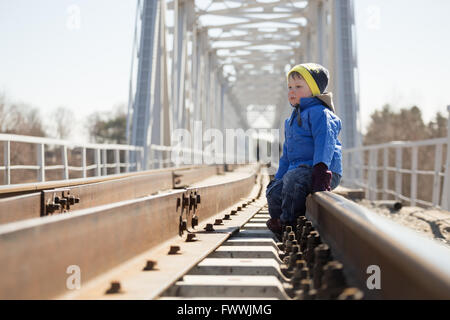 Ritratto di un ragazzino seduto sulle rotaie nelle ore diurne. Bielorussia Foto Stock