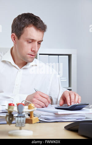 Uomo d'affari alla sua scrivania utilizzando una calcolatrice in ufficio Foto Stock