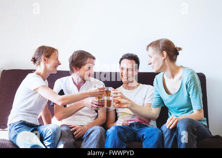 Gruppo di amici il tifo a casa felice giovane popolo sorridente con bevande, copyspace Foto Stock