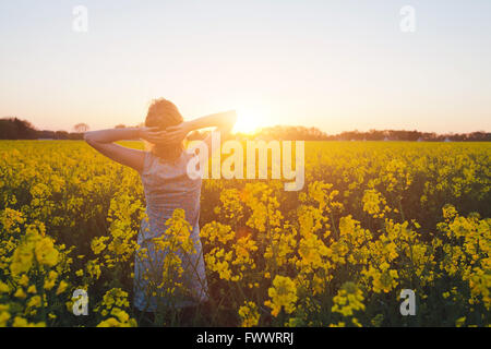 Giovane donna godendo di estate e la natura in fiore giallo campo al tramonto, armonia e stile di vita sano Foto Stock