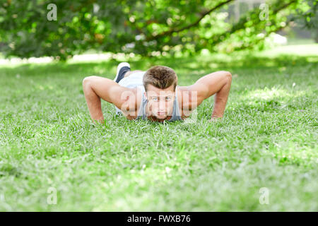 Giovane uomo che fa spingere ups su erba in estate park Foto Stock