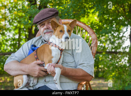 Ritratto di giovane basenji e senior uomo seduto in una sedia di vimini nel parco Foto Stock