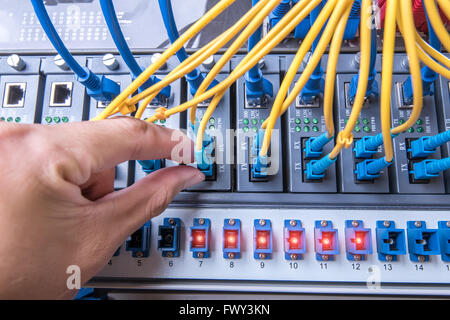 Uomo che lavora nel server del network camera con fibra ottica hub per le comunicazioni digitali e internet Foto Stock