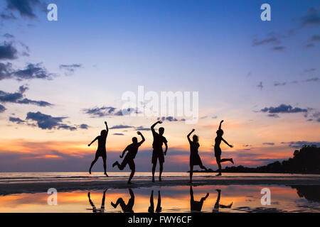 Gruppo di persone che saltano sulla spiaggia al tramonto, silhouette di amici divertendosi insieme