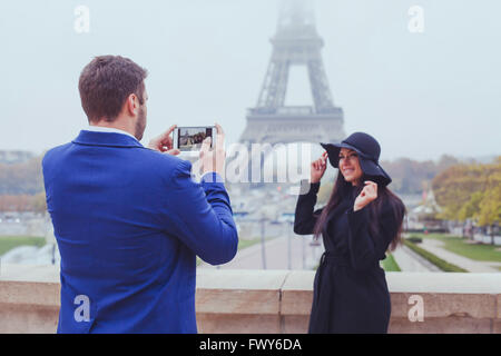 Fotografia mobile, uomo prendendo foto di donna con il suo telefono cellulare, coppia di turisti vicino alla Torre Eiffel a Parigi, Francia Foto Stock