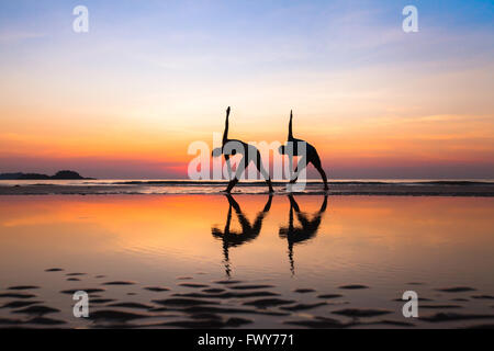 Stretchings sulla spiaggia al tramonto, esercizi di yoga, sagome di giovane Foto Stock