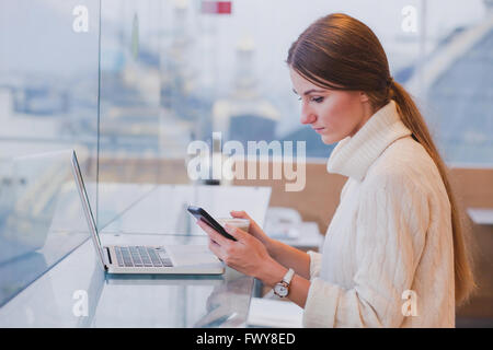 Donna che utilizza smart phone in moderno cafe inerior, applicazione per dispositivi mobili, il controllo della posta elettronica Foto Stock