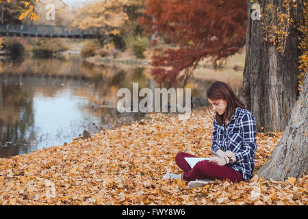 Concetto di lettura, giovane donna con libro in autunno park Foto Stock