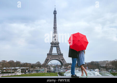 Luna di miele a Parigi, giovane kissing dietro red ombrello contro la Torre Eiffel Foto Stock