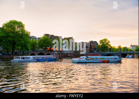 Amsterdam, Paesi Bassi. Una barca coperta in crociera al tramonto per i turisti con la bei canali della Binnen Fiume Amstel Foto Stock