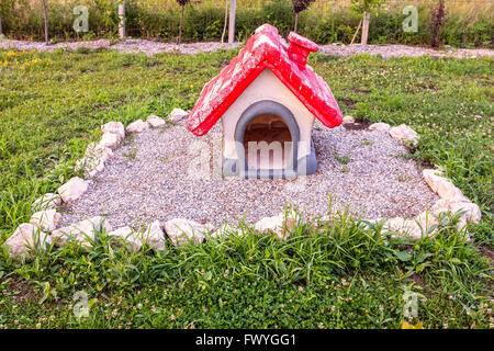 Casa del cane con un tetto rosso posto sulla tomba di un cane in un cimitero di Pet Foto Stock