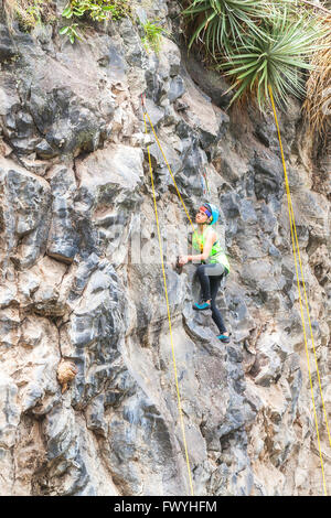 Banos, Ecuador - 30 Novembre 2014: la sfida di basalto del Tungurahua, gioventù ispanica scalatore di eseguire un esercizio di salvataggio di arrampicata Foto Stock