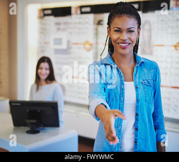 Piuttosto giovane americano africano all'ottico optometrista salutare un cliente presso la porta con un raggiante sorriso e la mano tesa o offerta Foto Stock