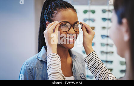 Attraente giovane donna africana scelta di occhiali con l aiuto di un all'ottico optometrista in un negozio cercando su diversi frame Foto Stock