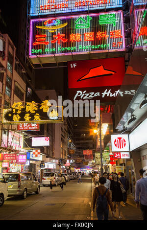 Le persone e le automobili in una strada piena di negozi e dei ristoranti di Tsim Sha Tsui, Hong Kong, Cina, di notte. Foto Stock