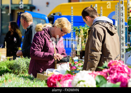 Simrishamn, Svezia - Aprile 1, 2016: Senior donna sta pagando per qualcosa, cerca di contanti nel suo portafoglio. Venditore di sesso maschile è in attesa Foto Stock