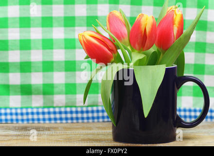 Rosso e tulipani gialli in blu navy mug sul fondo a scacchi con spazio di copia Foto Stock