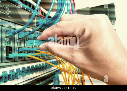 Mano con rete in fibra di cavi collegati al server di un data center Foto Stock