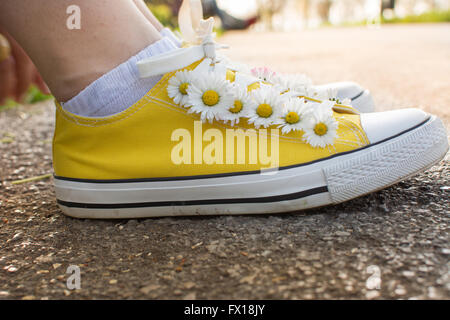 Sneakers giallo decorato con margherite nel parco Foto Stock