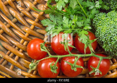 Pomodorini con prezzemolo e broccoli su un piatto di legno Foto Stock