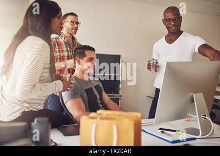 Gruppo diversificato di maschio e femmina adulti imprenditori radunati intorno a grandi monitor del computer sulla scrivania per sale riunioni Foto Stock