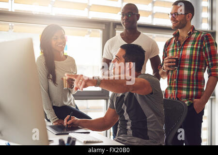 Uomo con stilo e tablet mostrando qualcosa sul suo computer a un gruppo di tre maschi e femmine casualmente vestito co-lavoratori hol Foto Stock